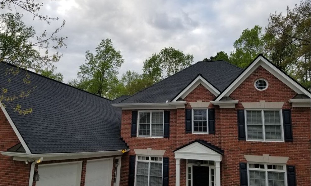Completed dark-gray shingle roof on a two-story brick home with white trim