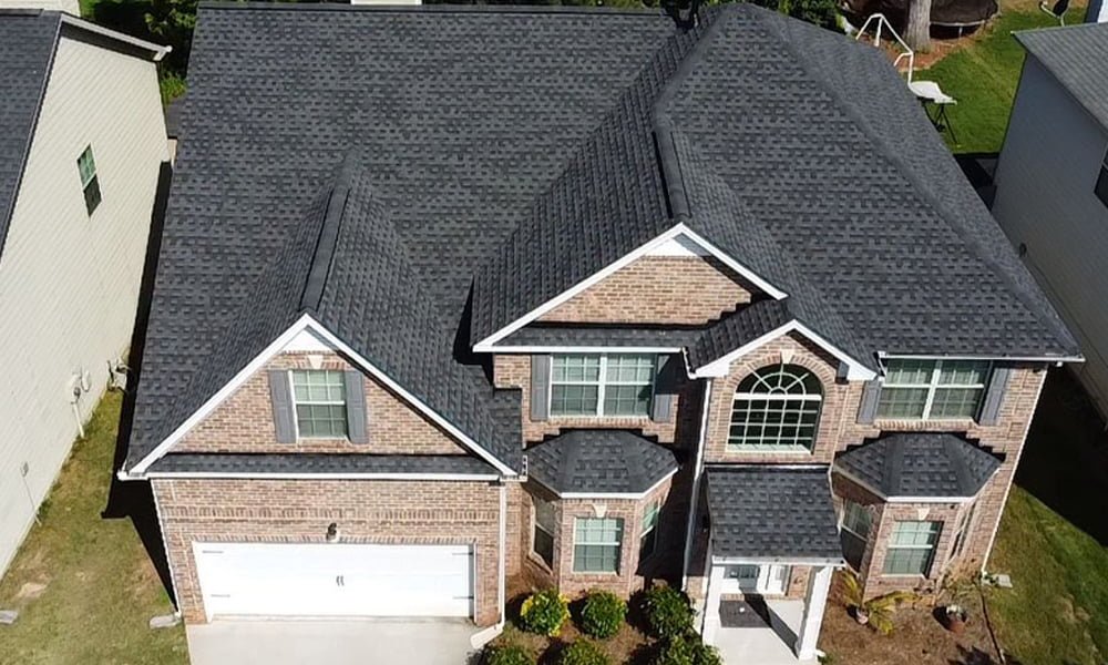 Aerial view of a completed architectural shingle roof on a two-story brick house