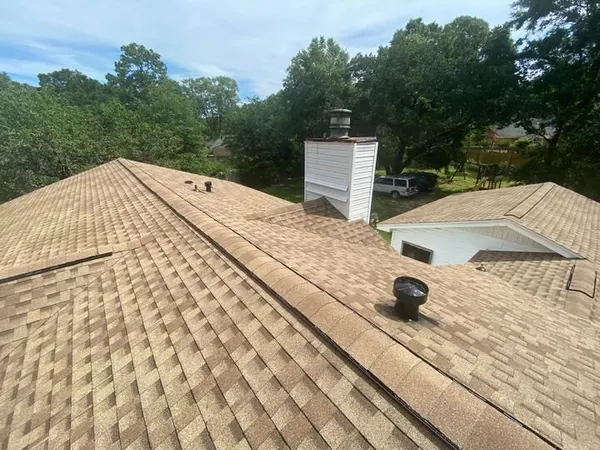 Finished tan architectural shingles along a roof ridge and chimney