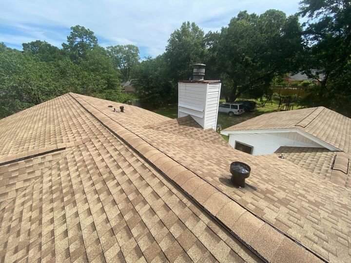 Finished tan architectural shingles along a roof ridge and chimney